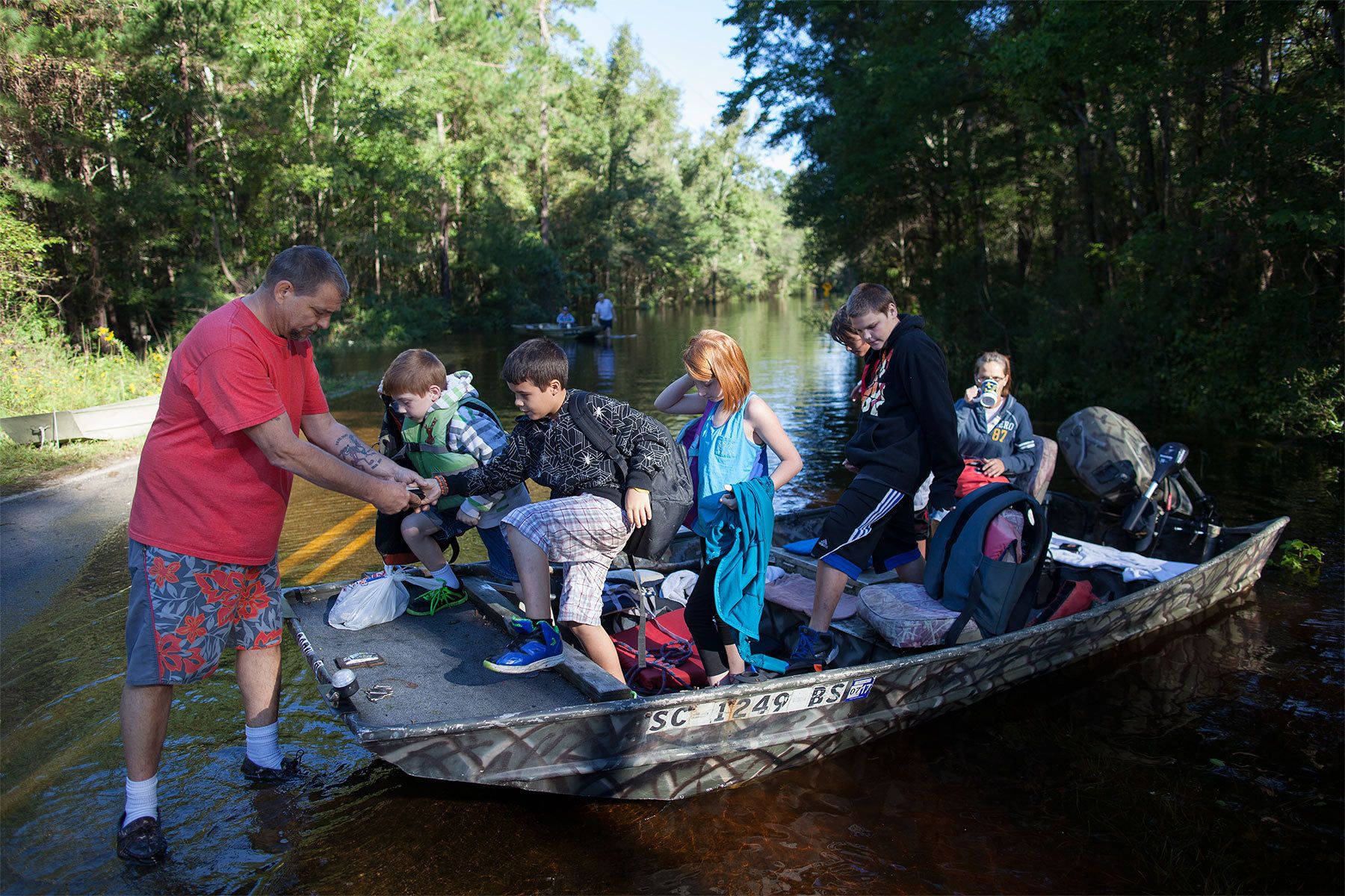 Scott Everett (L) helps his grandchildren enroute to school off a johnboat along Lee's Landing Circle in Conway, South Carolina October 7, 2015. The family has been living in their home surrounded by flood waters since Sunday evening. Scott Everett (L) helps his grandchildren enroute to school off a johnboat along Lee's Landing Circle in Conway, South Carolina October 7, 2015. The family has been living in their home surrounded by flood waters since Sunday evening. Rescuers searched early Wednesday for two people missing in floodwaters in South Carolina, while authorities urged residents in hundreds of homes to seek higher ground. REUTERS/Randall Hill