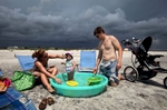 With storm clouds looming in the background, Charlotte, N.C., residents Mark and Denise Flanders and daughter Verity, enjoy their vacation August 24, 2011 on the east end of Ocean Isle Beach in southeastern North Carolina. The family has a rental house through Sunday but plan on leaving for home a day early if the winds and rain from Hurricane Irene spoil their travels to the coast. Hurricane Irene could pose a big threat to the densely populated northeast United States, including New York, as it swings up the eastern seaboard from Saturday on its current forecast track, the top U.S. government hurricane forecaster said on Wednesday.   For REUTERS and The New York Times